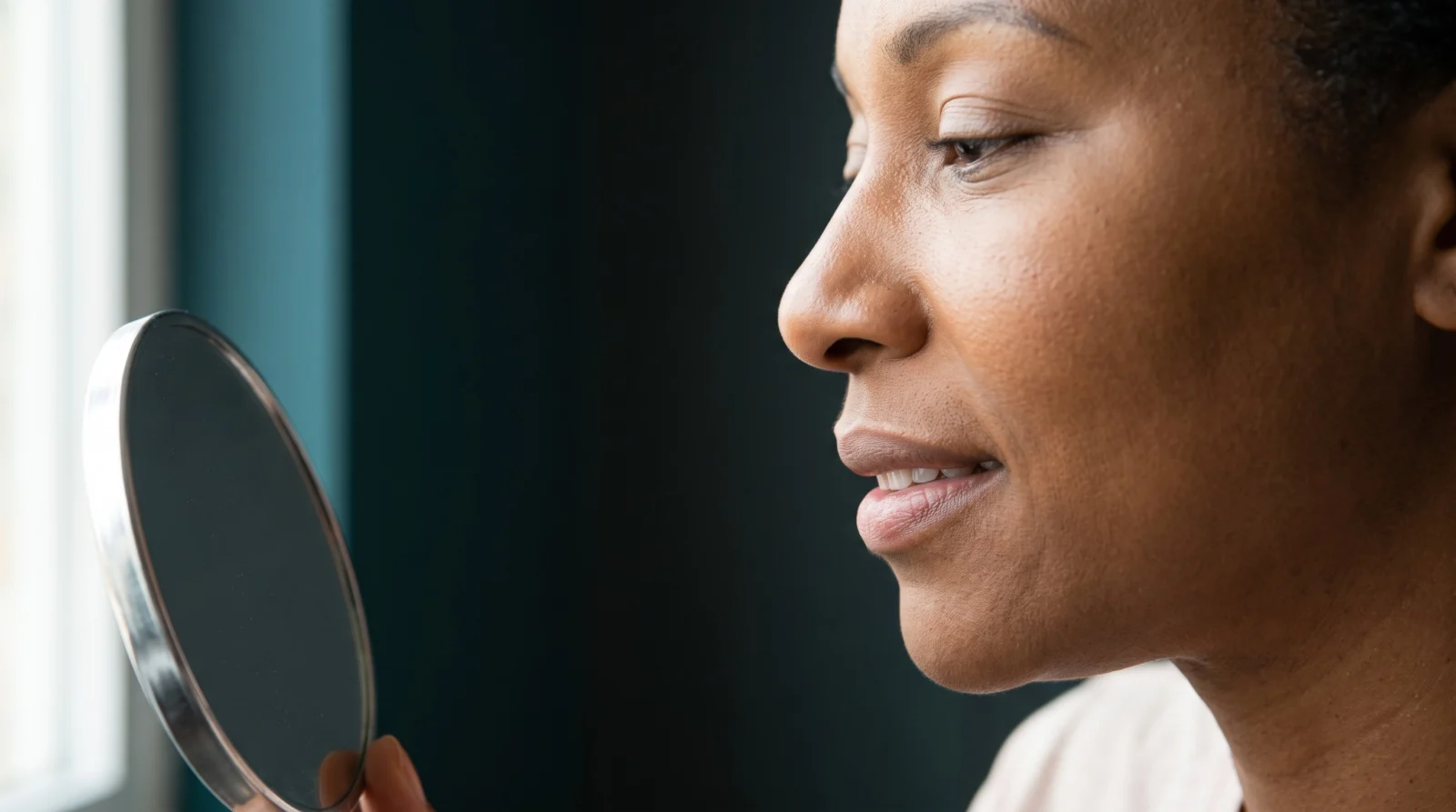 Black woman examining her upper lip and philtrum in a hand mirror