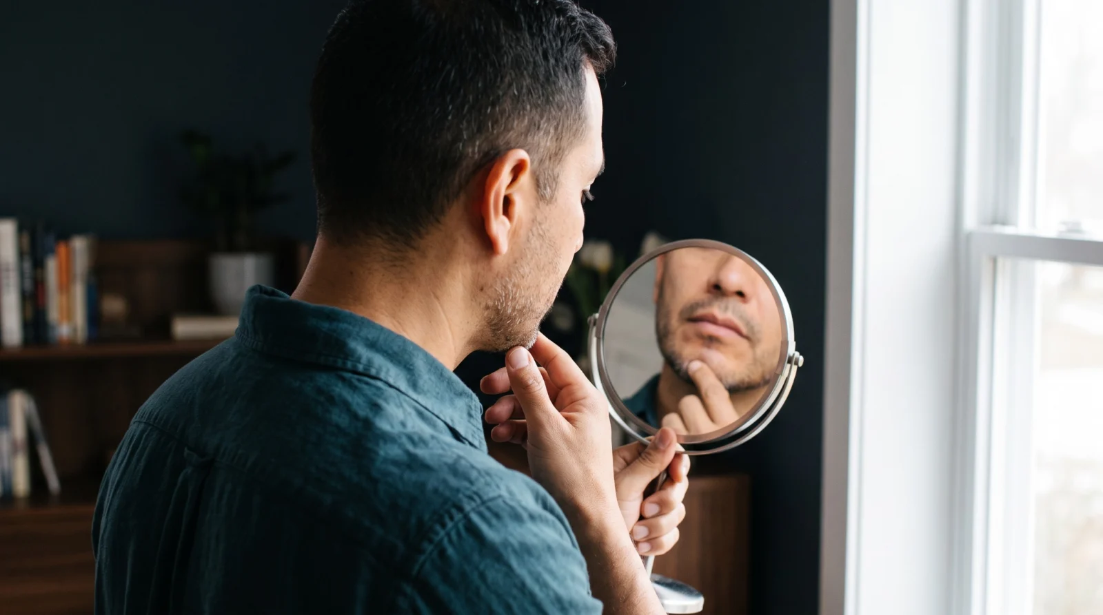 Man checking his chin contour in a round mirror during later recovery